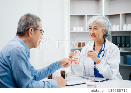 Concentrated dentist sitting at table with jaw samples tooth model and working with tablet and laptop in dental office professional dental clinic. medical doctor working 134280713