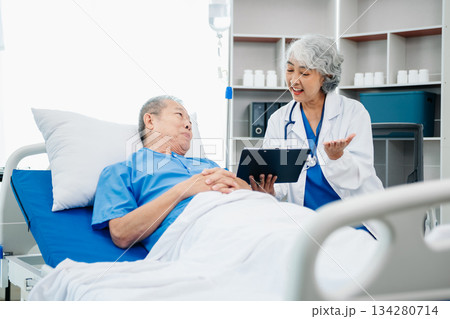 Asian doctor in white suit take notes while discussing and Asian elderly, man patient who lying on bed with receiving saline solution 134280714