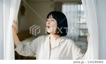 朝、窓のカーテンを開け光を浴びる女性 134280968