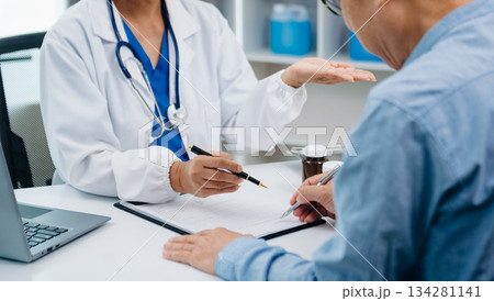 A professional physician talks to discuss results or symptoms and gives a recommendation to a male patient and signs a medical paper 134281141