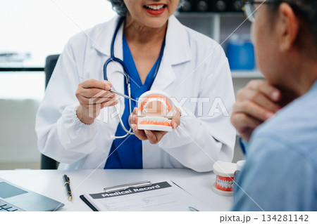 Concentrated dentist sitting at table with jaw samples tooth model and working with tablet and laptop in dental office professional dental clinic. medical doctor working Concentrated dentist sitting at table with jaw samples tooth model and working with tablet and laptop in dental office professional dental clinic. medical doctor working 134281142