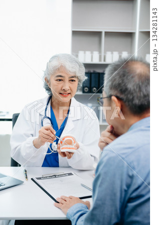 Concentrated dentist sitting at table with jaw samples tooth model and working with tablet and laptop in dental office professional dental clinic. medical doctor working Concentrated dentist sitting at table with jaw samples tooth model and working with tablet and laptop in dental office professional dental clinic. medical doctor working 134281143