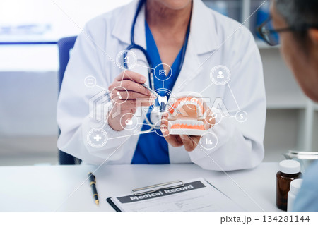 Concentrated dentist sitting at table with jaw samples tooth model and working with tablet and laptop in dental office professional dental clinic. medical doctor working Concentrated dentist sitting at table with jaw samples tooth model and working with tablet and laptop in dental office professional dental clinic. medical doctor working 134281144