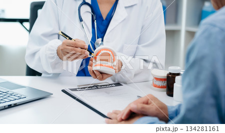 Concentrated dentist sitting at table with jaw samples tooth model and working with tablet and laptop in dental office professional dental clinic. medical doctor working Concentrated dentist sitting at table with jaw samples tooth model and working with tablet and laptop in dental office professional dental clinic. medical doctor working 134281161