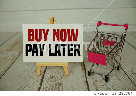Buy Now Pay Later text on paper card and trolley shopping cart on wooden background 134281764