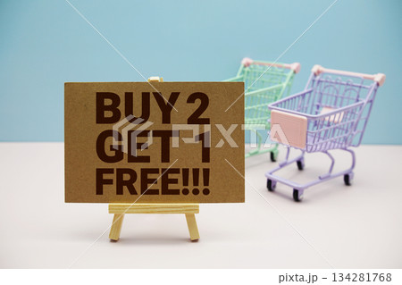 Buy 2 Get 1 Free!!! text on paper card and trolley shopping cart on pastel background 134281768