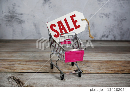 Mini Shopping Cart with Sale Price Tag on Wooden Background Mini Shopping Cart with Sale Price Tag on Wooden Background 134282024