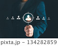 Businessman holding magnifying glass focusing on candidate icon, symbolizing recruitment, human resources, employee selection, target audience, and business hiring strategy. 134282859