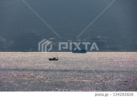 日の光に輝く海面に浮かぶ漁船と遠くの大型船 134283826