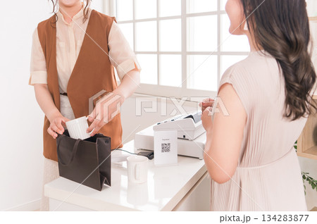 アパレルショップ・雑貨屋のレジで商品を渡すショップ店員と受け取る女性客 134283877