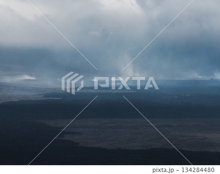 Dramatic aerial view of dark lava fields in Iceland, with steam rising from geothermal activity and heavy clouds creating a moody atmosphere. 134284480