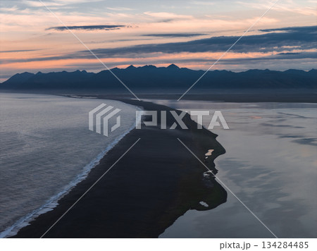 Aerial view of a black sand beach in Iceland with calm waters, jagged mountains, and a pastel sunset sky creating a dramatic landscape. Aerial view of a black sand beach in Iceland with calm waters, jagged mountains, and a pastel sunset sky creating a dramatic landscape. 134284485