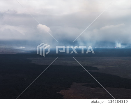Dark volcanic terrain with rising steam plumes, showcasing geothermal activity under an overcast sky in Iceland's rugged natural environment. 134284519