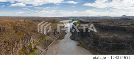 Dettifoss waterfall in Iceland cascades into a rugged canyon, surrounded by basalt cliffs, rocky terrain, green patches, and mist under a cloudy sky. Dettifoss waterfall in Iceland cascades into a rugged canyon, surrounded by basalt cliffs, rocky terrain, green patches, and mist under a cloudy sky. 134284652