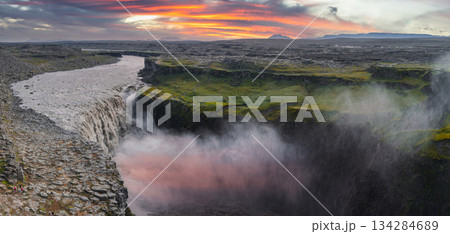 Dettifoss waterfall cascades into a misty canyon, surrounded by cliffs and moss, under a vibrant sunset with orange, pink, and purple hues. Dettifoss waterfall cascades into a misty canyon, surrounded by cliffs and moss, under a vibrant sunset with orange, pink, and purple hues. 134284689