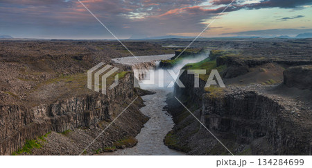 Dettifoss waterfall cascades powerfully into a rugged canyon carved by the Jokulsa a Fjollum river, with mist rising under a pastel colored sky. Dettifoss waterfall cascades powerfully into a rugged canyon carved by the Jokulsa a Fjollum river, with mist rising under a pastel colored sky. 134284699