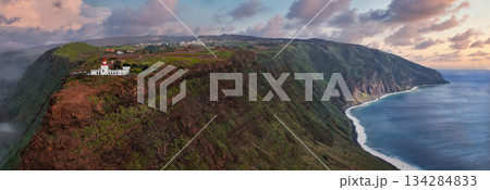 Aerial view shows Miradouro Farol da Ponta do Pargo, Madeira, Portugal, on a sheer cliff above the Atlantic, with beach, fields, pastel light, and long headlands Aerial view shows Miradouro Farol da Ponta do Pargo, Madeira, Portugal, on a sheer cliff above the Atlantic, with beach, fields, pastel light, and long headlands 134284833