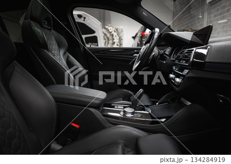 Black leather seats with quilted pattern, high tech dashboard, and carbon fiber accents in a modern car. Background shows a car shop setting. Black leather seats with quilted pattern, high tech dashboard, and carbon fiber accents in a modern car. Background shows a car shop setting. 134284919
