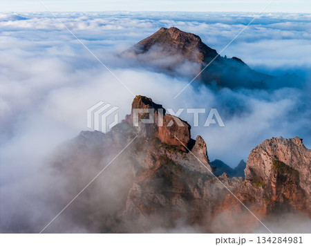 Aerial view shows rugged reddish peaks and ridgelines near Pico do Arieiro in Madeira, Portugal, as soft sunrise light casts subtle shadows across misty summits. Aerial view shows rugged reddish peaks and ridgelines near Pico do Arieiro in Madeira, Portugal, as soft sunrise light casts subtle shadows across misty summits. 134284981