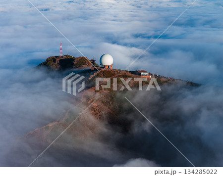 Aerial view of Pico do Arieiro on Madeira Island, radar dome and tower on rugged summit, soft low light, brown volcanic rock, clouds swirl around the peak 134285022