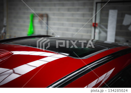 The sunroof and roofline of a red luxury car, likely a BMW X4, in a garage with a gray brick wall, tools, and a green cover in the background. The sunroof and roofline of a red luxury car, likely a BMW X4, in a garage with a gray brick wall, tools, and a green cover in the background. 134285024