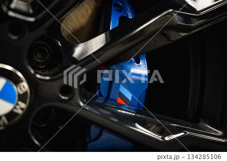 Detailed view of a BMW M series wheel featuring a glossy black alloy rim and blue brake caliper with the iconic tri color M logo in a showroom setting. Detailed view of a BMW M series wheel featuring a glossy black alloy rim and blue brake caliper with the iconic tri color M logo in a showroom setting. 134285106