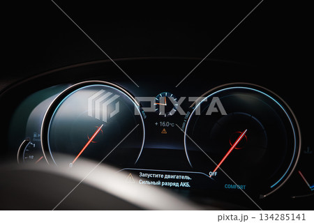 Close up of a BMW dashboard showing speedometer, tachometer, and digital display in Russian with engine start message and battery warning. Close up of a BMW dashboard showing speedometer, tachometer, and digital display in Russian with engine start message and battery warning. 134285141