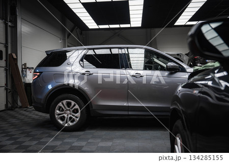 A silver Range Rover Discovery is parked on a checkered floor in a well lit garage with industrial design, tools, and part of a black BMW visible. 134285155