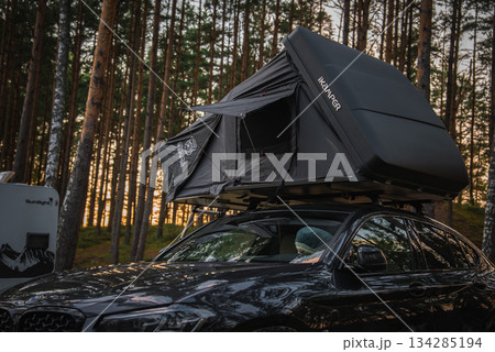 A black BMW X4 2025 with an IKAMPER rooftop tent parked in a forested area. Tall pine trees and a camper van are visible during a warm sunset. A black BMW X4 2025 with an IKAMPER rooftop tent parked in a forested area. Tall pine trees and a camper van are visible during a warm sunset. 134285194