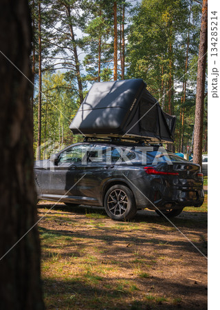 A BMW X4 2025 parked in a forest surrounded by tall pine trees, with a rooftop tent partially open under sunlight filtering through the branches. A BMW X4 2025 parked in a forest surrounded by tall pine trees, with a rooftop tent partially open under sunlight filtering through the branches. 134285214