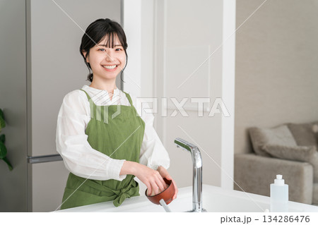 キッチンのシンクで洗い物をするエプロン姿の若いアジア人女性 キッチンのシンクで洗い物をするエプロン姿の若いアジア人女性 134286476