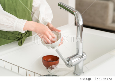 キッチンのシンクで洗い物をするエプロン姿の若いアジア人女性の手元 キッチンのシンクで洗い物をするエプロン姿の若いアジア人女性の手元 134286478