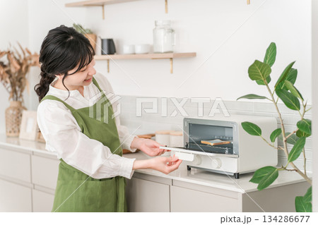 キッチンでトースターを使うエプロン姿の主婦,若いアジア人女性 キッチンでトースターを使うエプロン姿の主婦,若いアジア人女性 134286677
