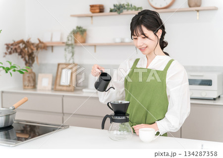 キッチンでコーヒーをいれるエプロン姿の若いアジア人女性 キッチンでコーヒーをいれるエプロン姿の若いアジア人女性 134287358