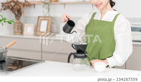 キッチンでコーヒーをいれるエプロン姿の若いアジア人女性 キッチンでコーヒーをいれるエプロン姿の若いアジア人女性 134287359