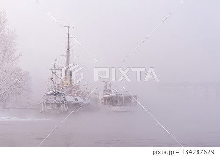 Atmospheric foggy landscape with nostalgic mood. Old decommissioned vessels, a Jung river tram and a tugboat or a river icebreaker permanently parked on the Yenisei River, shrouded in mystery and fog 134287629