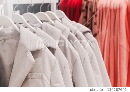 Coats and jackets hang neatly on display in a clothing store. Colors range from gray to shades of red. Coat hangers in a clothing store. Seasonal purchase of warm demi-season clothes for spring, Coats and jackets hang neatly on display in a clothing store. Colors range from gray to shades of red. Coat hangers in a clothing store. Seasonal purchase of warm demi-season clothes for spring, 134287643
