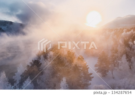 Sunlight breaks through misty clouds, reflecting on snowy trees in Krasnoyarsk, Russia, marking the New Year season in Siberia. Nature showcases its winter beauty in peaceful surroundings. High 134287654