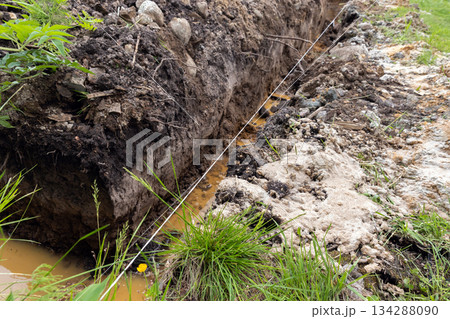 A trench filled with water surrounded by mud and grass A trench filled with water surrounded by mud and grass 134288090