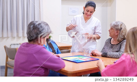 Caregiver serving water to senior women playing board game 134289249