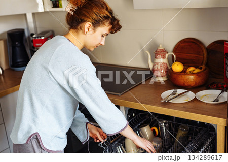 young woman putting dirty dishes into dishwasher at home young woman putting dirty dishes into dishwasher at home 134289617