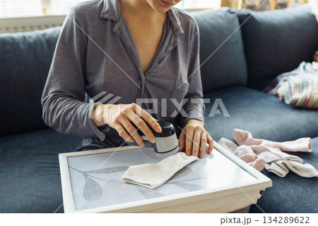 woman takes care of clothes at home, cuts off lint with tool 134289622