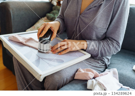 woman takes care of clothes at home, cuts off lint with tool 134289624