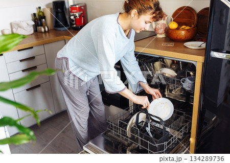 young woman putting dirty dishes into dishwasher at home young woman putting dirty dishes into dishwasher at home 134289736