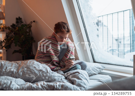 young woman warms up with hot tea in winter weather at home young woman warms up with hot tea in winter weather at home 134289755