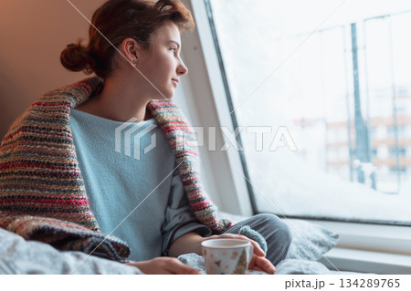 young woman warms up with hot tea in winter weather at home young woman warms up with hot tea in winter weather at home 134289765