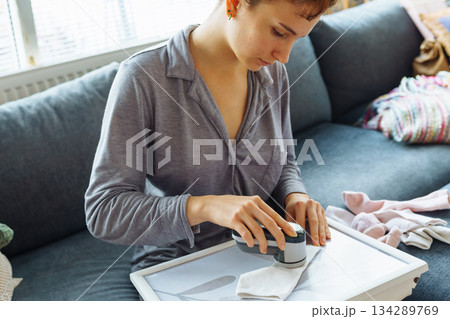 woman takes care of clothes at home, cuts off lint with tool 134289769