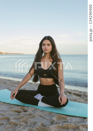 Woman meditating on yoga mat by the sea, yoga meditation, wellness routine, mindfulness practice, beach fitness, calm breathing, relaxing seaside yoga session at sunrise. Woman meditating on yoga mat by the sea, yoga meditation, wellness routine, mindfulness practice, beach fitness, calm breathing, relaxing seaside yoga session at sunrise. 134290400