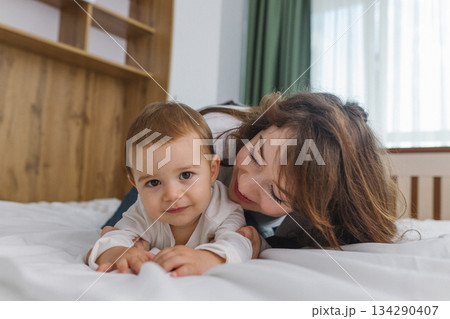 Young mother playing with her baby at home, enjoying a warm and cozy family moment full of tenderness, comfort, natural light, and playful parent-child connection. Young mother playing with her baby at home, enjoying a warm and cozy family moment full of tenderness, comfort, natural light, and playful parent-child connection. 134290407