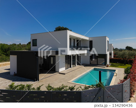 Modern luxury villa with swimming pool and clean minimalist architecture under a blue sky. Contemporary residential exterior featuring large windows, terrace, and elegant outdoor living space 134290436